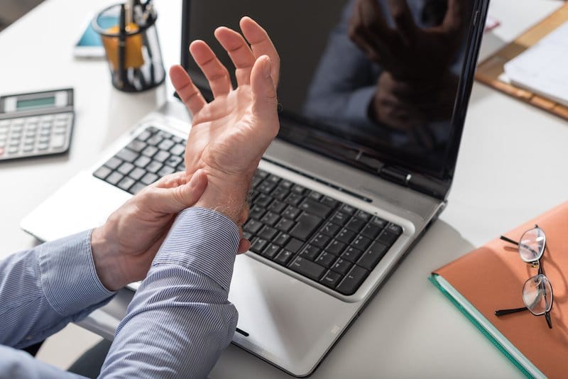 man at laptop with repetitive strain injury stretching wrist