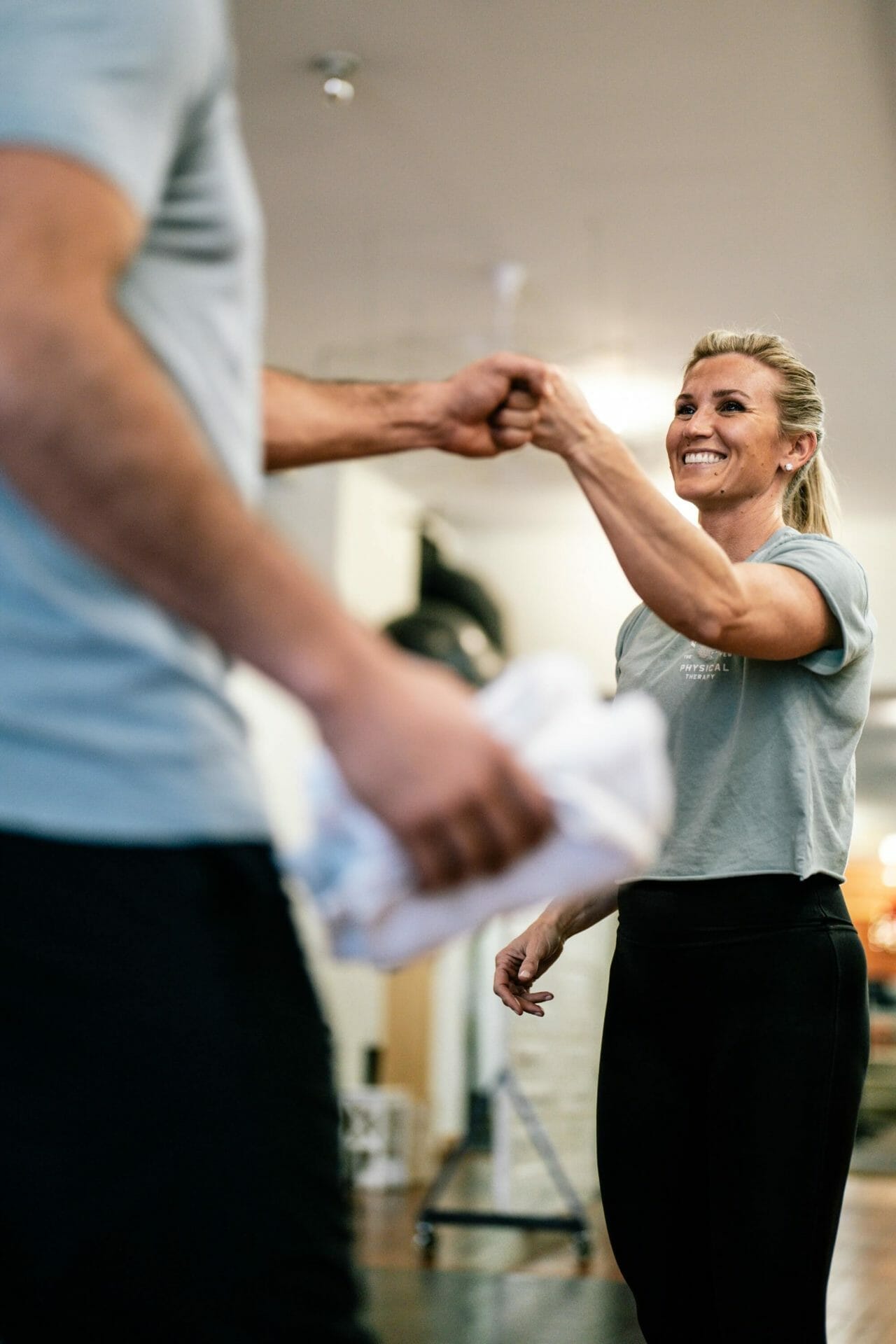 The therapist is smiling while giving her client a fist bump