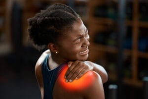 A woman touching her shoulder in discomfort, indicating pain.