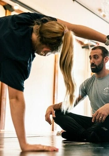 a man sitting down on the floor while watching a woman doing the physical therapy posture exercise